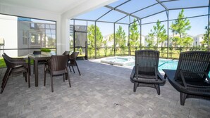 Área de varanda coberta com estrutura de vidro, mobiliário externo e vista para uma piscina e vegetação.