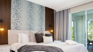 Quarto moderno com uma cama grande, mesa de cabeceira e vista para o exterior através de uma porta de vidro.