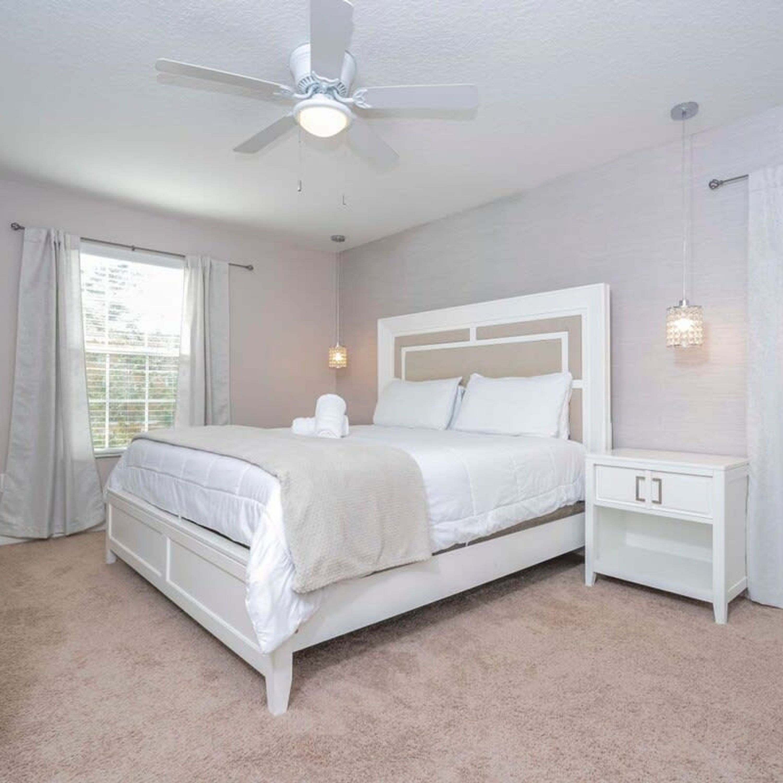A bedroom with a bed, nightstands, a ceiling fan, and a window with curtains.