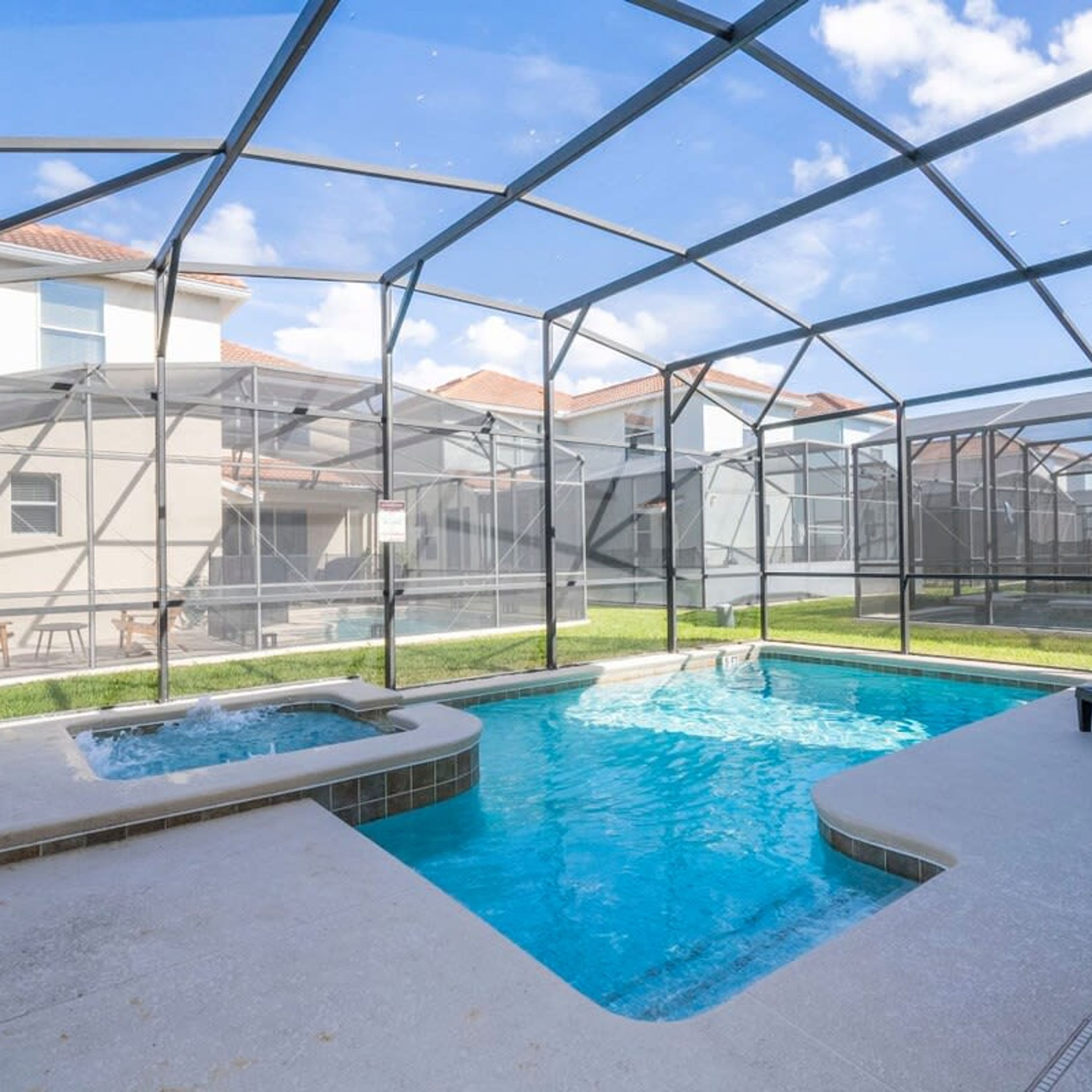 A swimming pool with a hot tub, surrounded by a covered area with a metal frame and mesh walls.