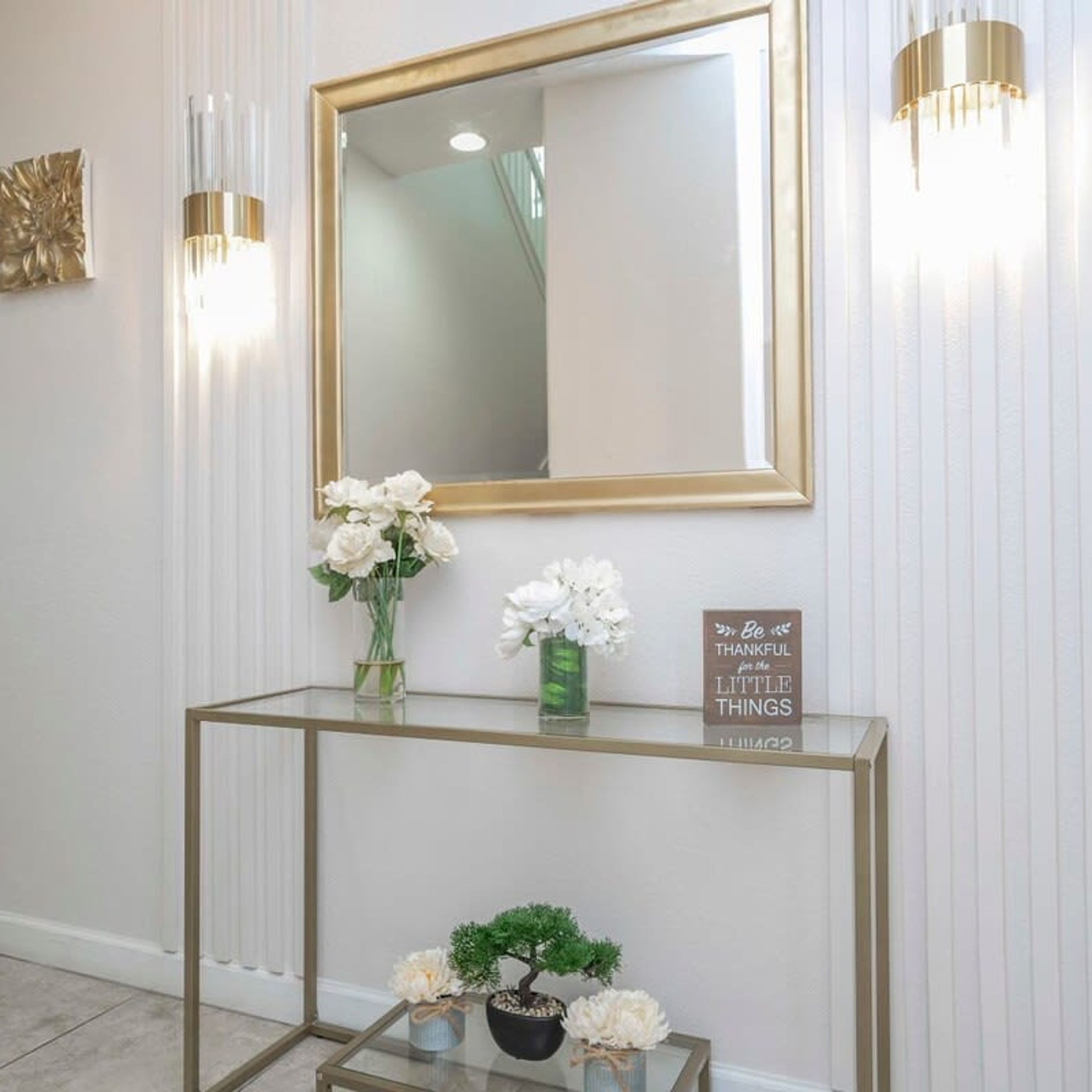 A hallway with a glass console table, a mirror, and two wall-mounted lights.