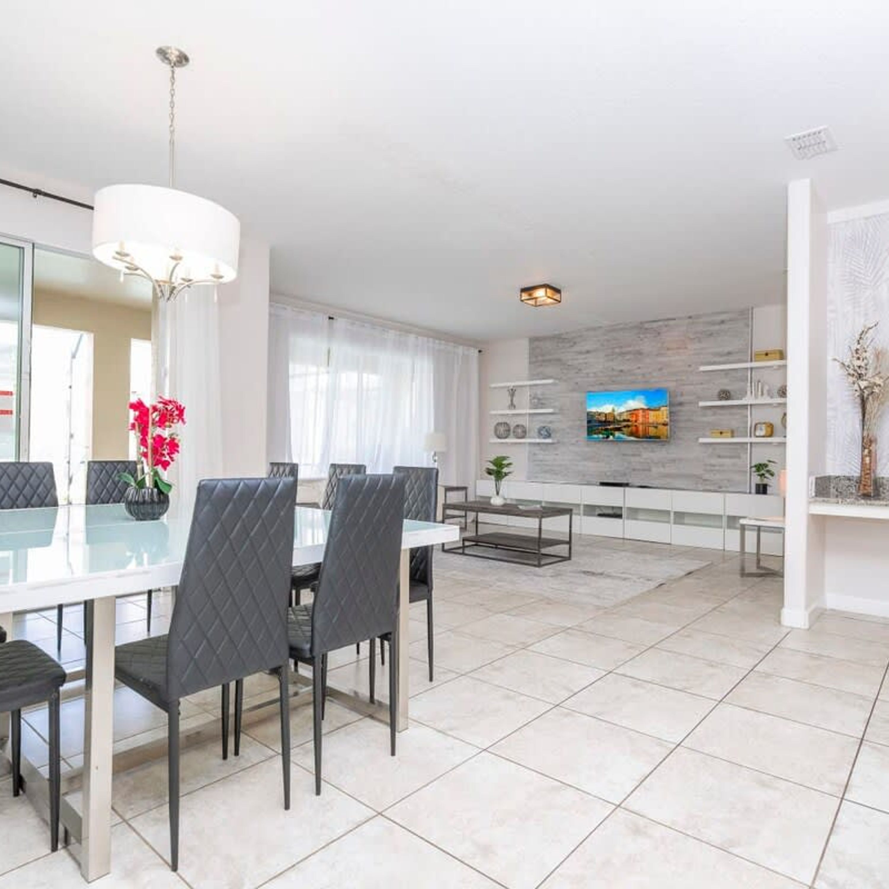 A modern living room with a dining area, a TV mounted on the wall, and a minimalist design.