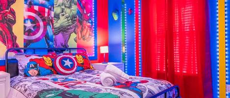 A bedroom with a bed featuring superhero-themed bedding, a wall mural with comic book characters, and red curtains with a vertical light strip.