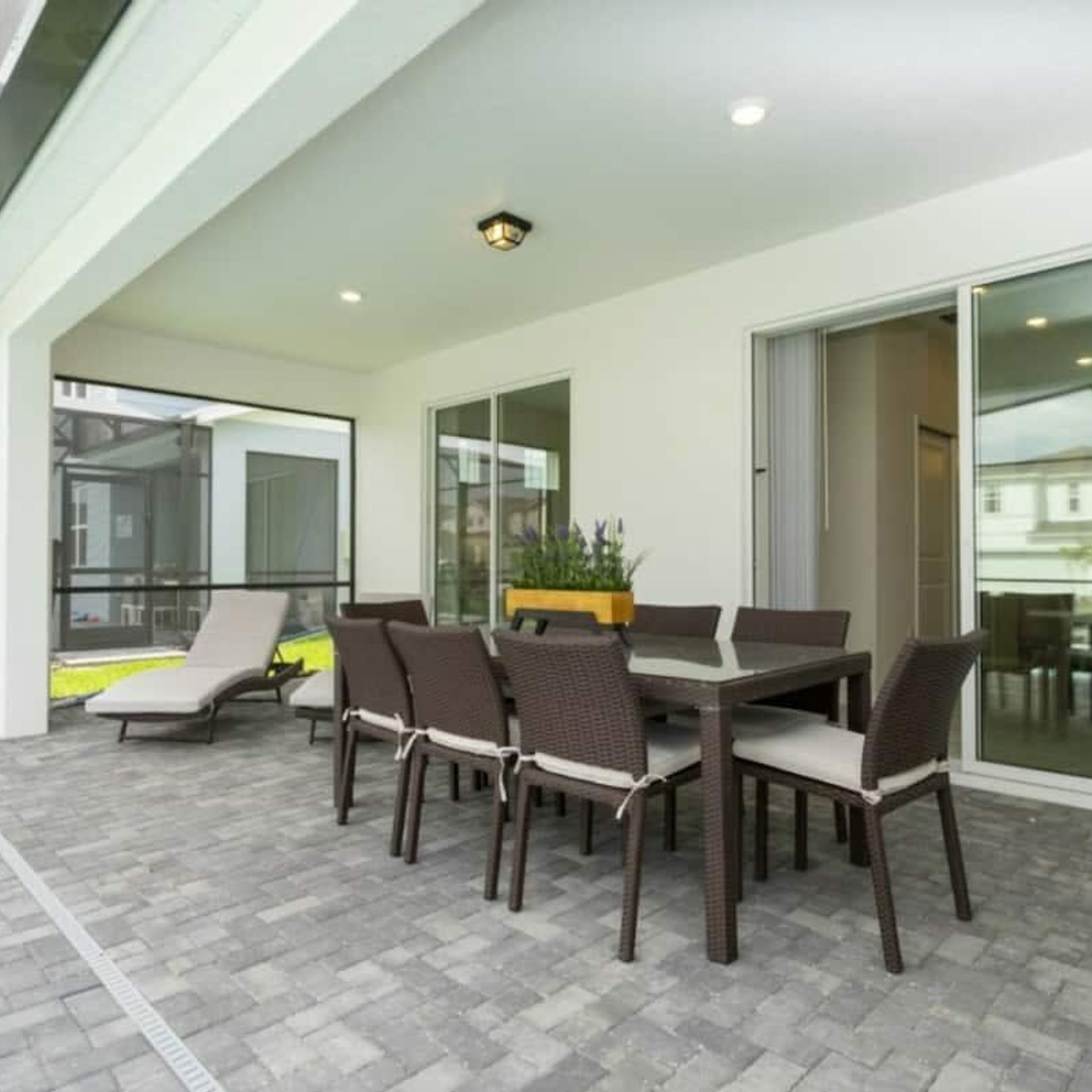A covered patio with a table and chairs, a potted plant, and a glass door leading to an interior space.