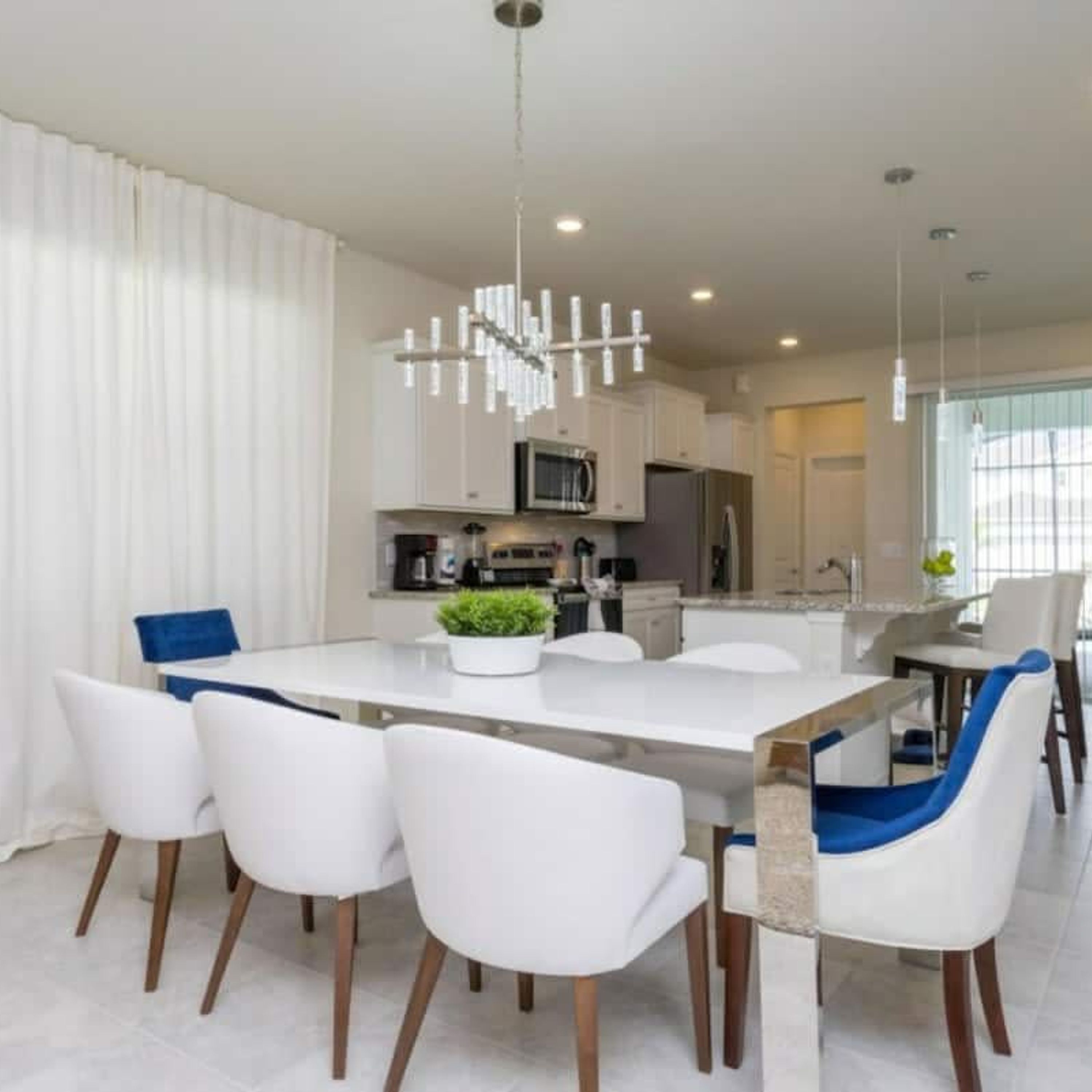 A modern kitchen with white cabinetry, a central island, and a dining area with white chairs and a blue accent.