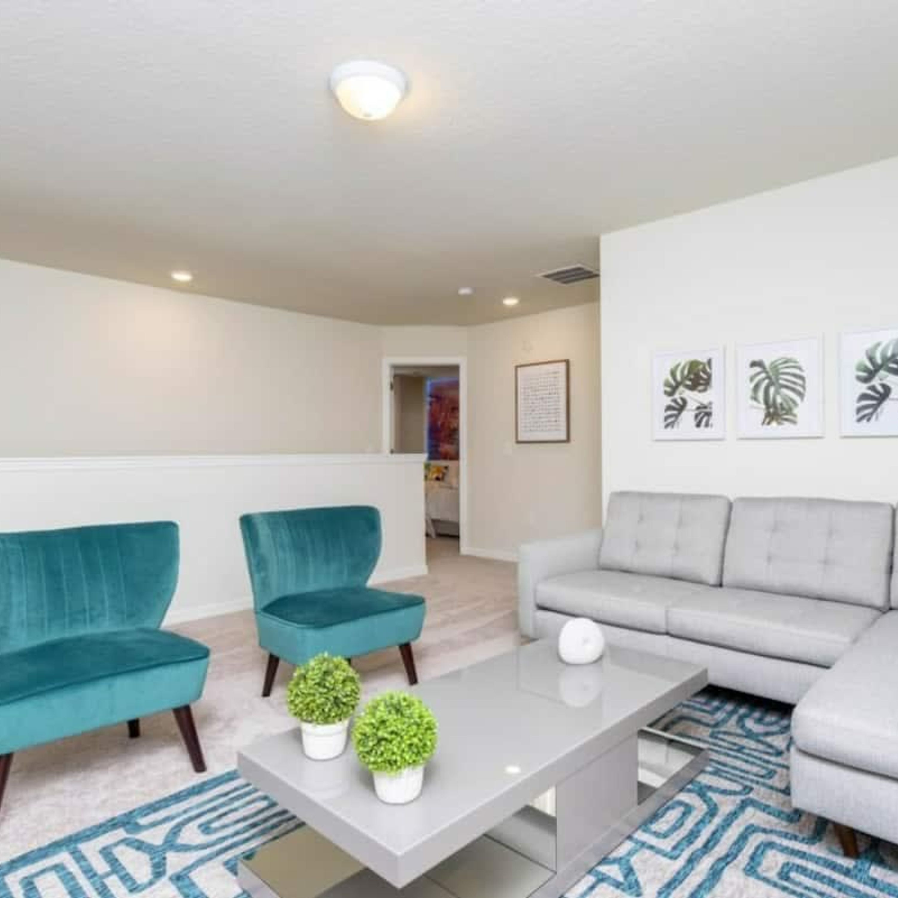 A modern living room with teal and grey sofas, a coffee table with potted plants, and framed botanical prints on the wall.