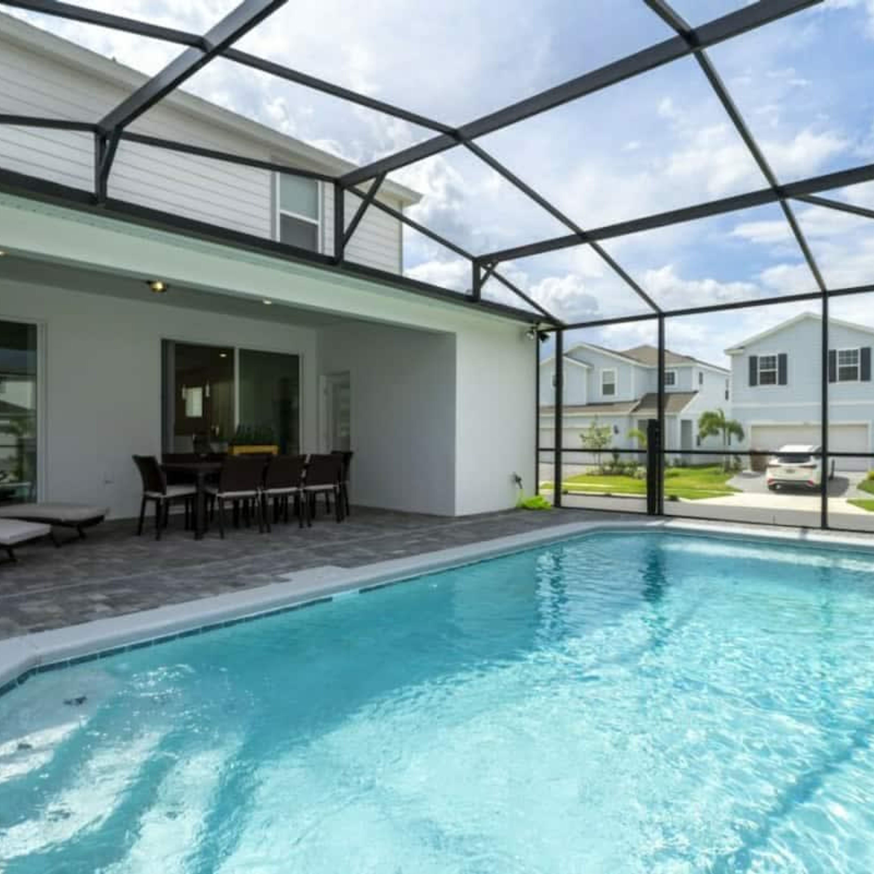 Ein Schwimmbad mit überdachter Terrasse, einem Tisch mit Stühlen und Blick auf umliegende Häuser.