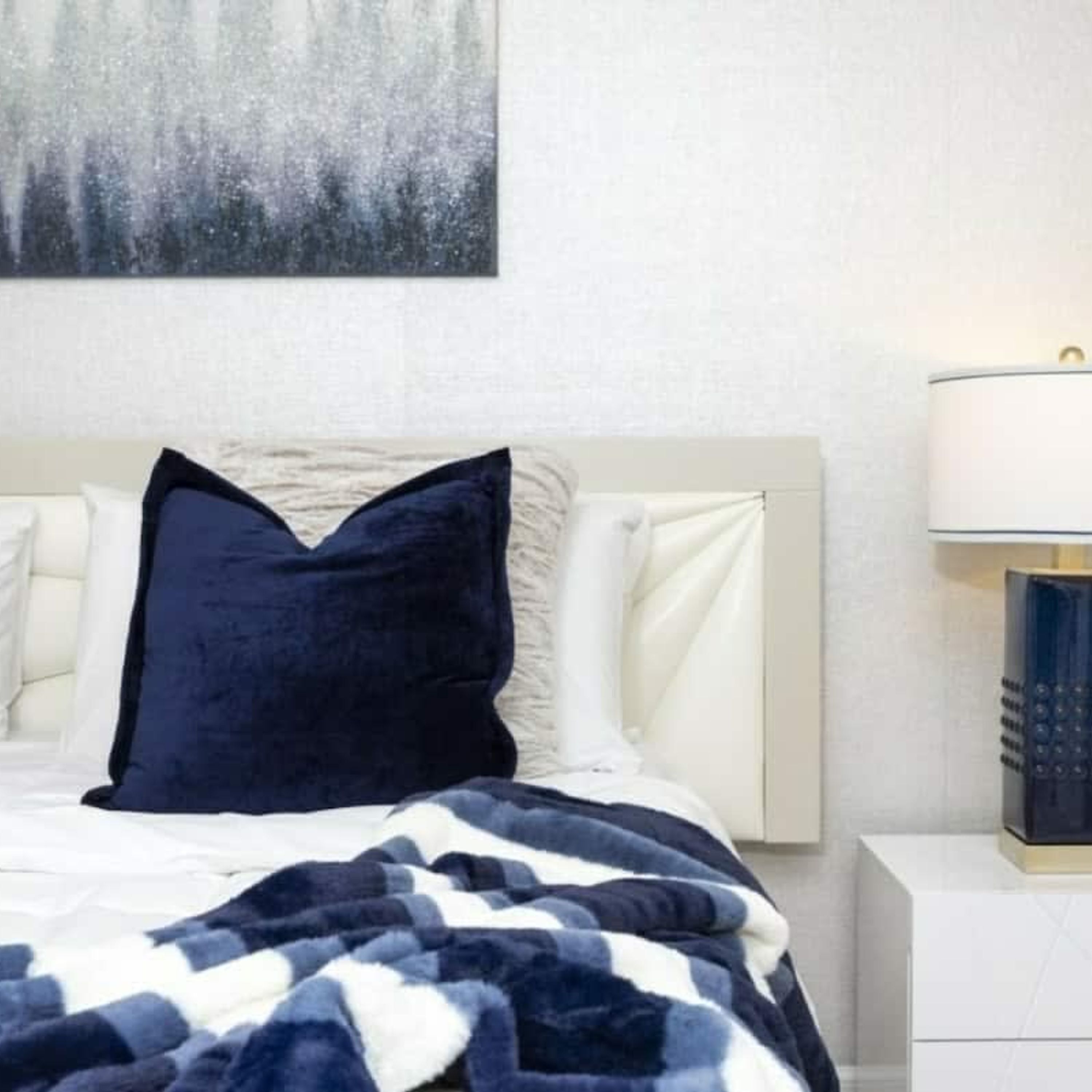 A bed with a dark blue pillow and a blue and white checkered blanket.