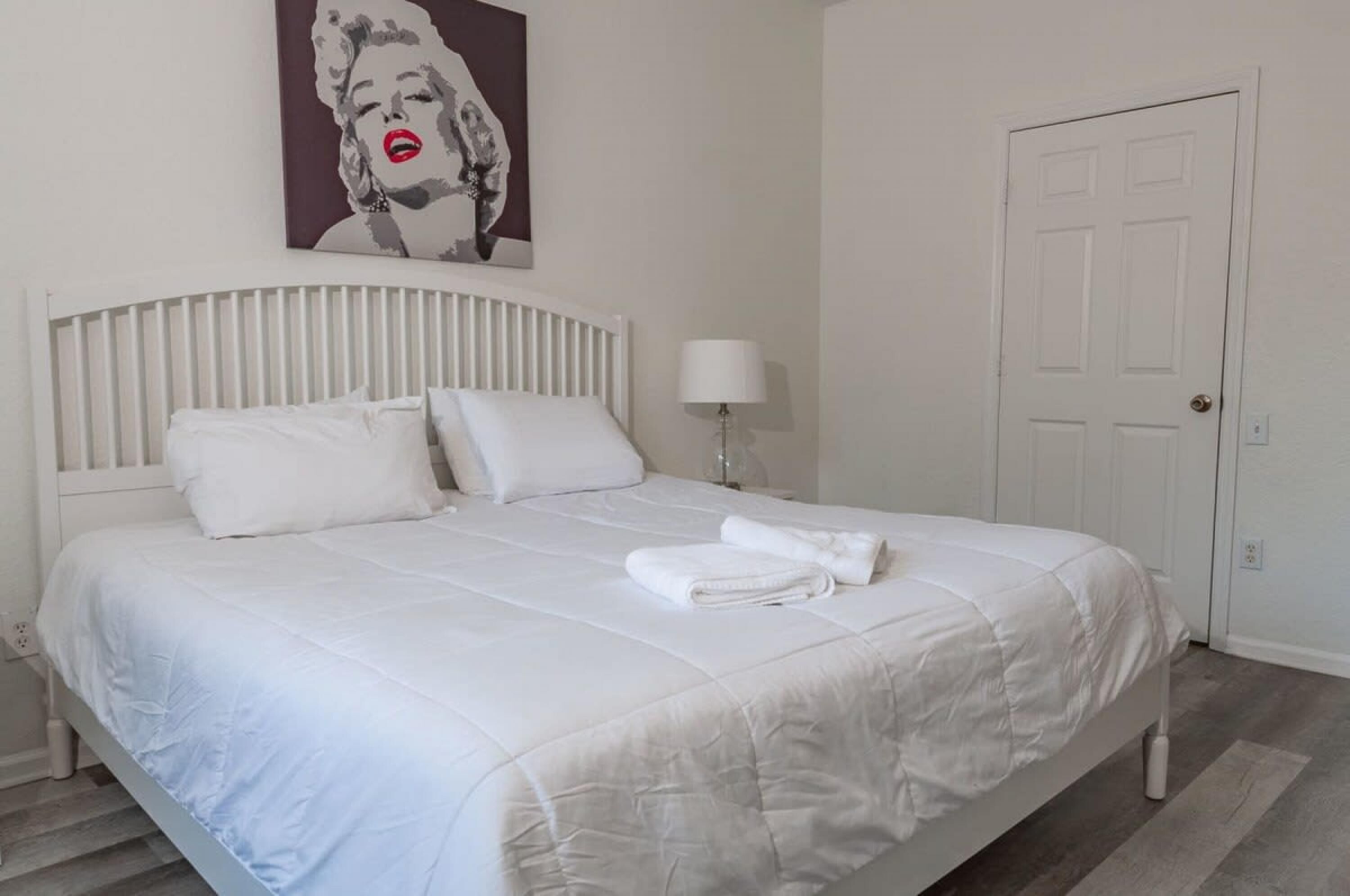 A neatly made bed with white bedding, a white headboard, and a white door in the background.
