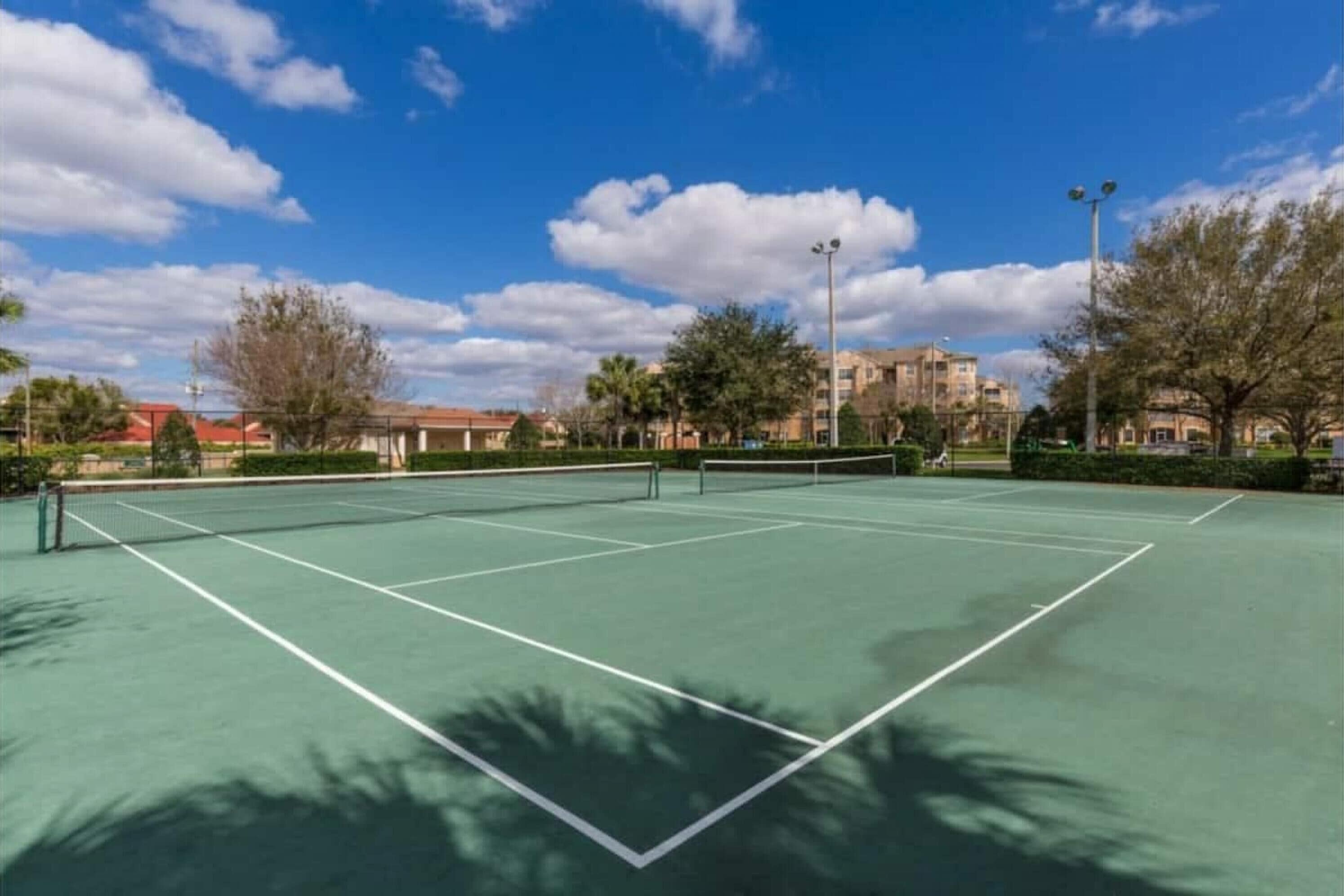 A tennis court with a net, surrounded by trees and buildings.