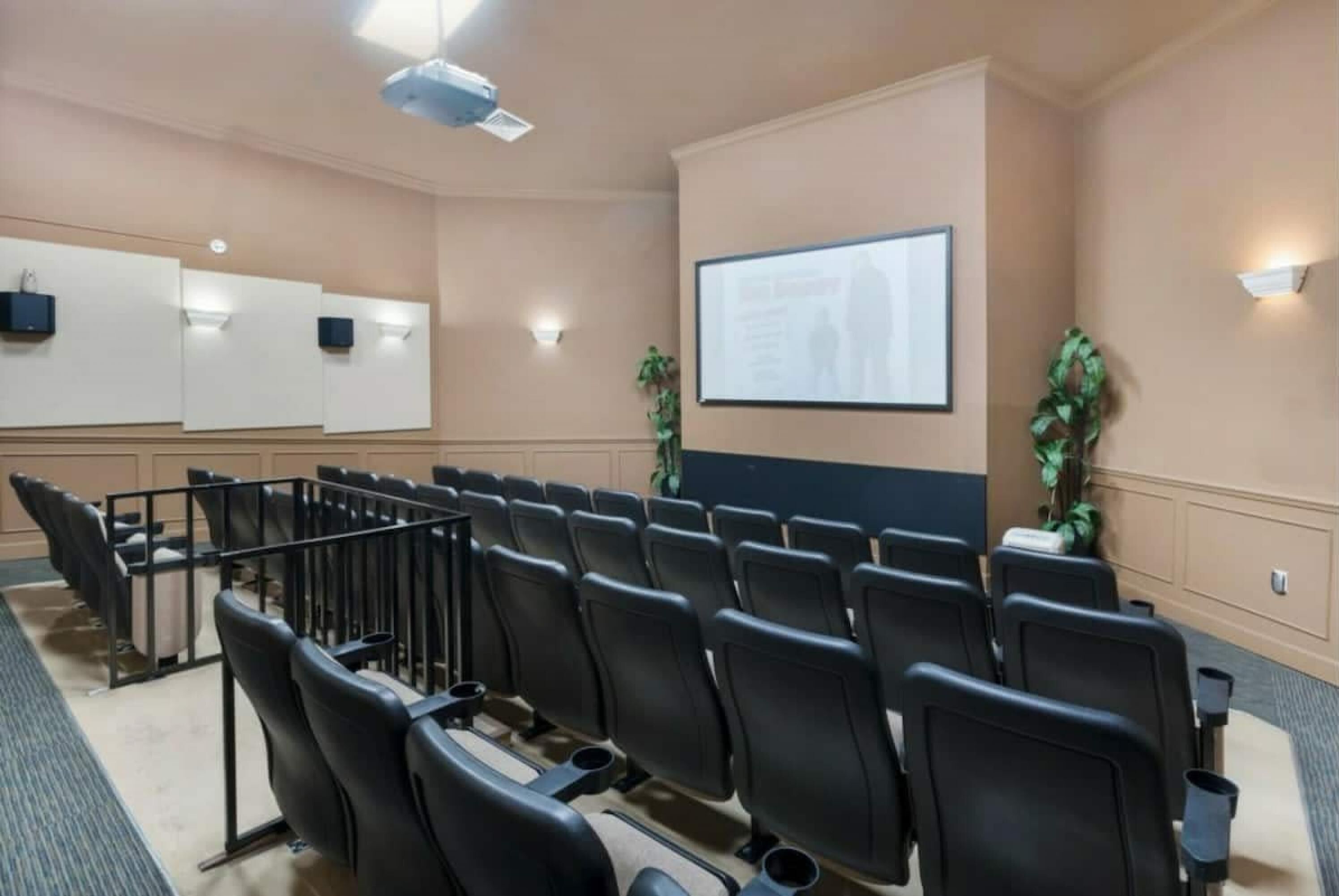 A conference room with rows of black chairs, a projector screen, and two wall-mounted speakers.