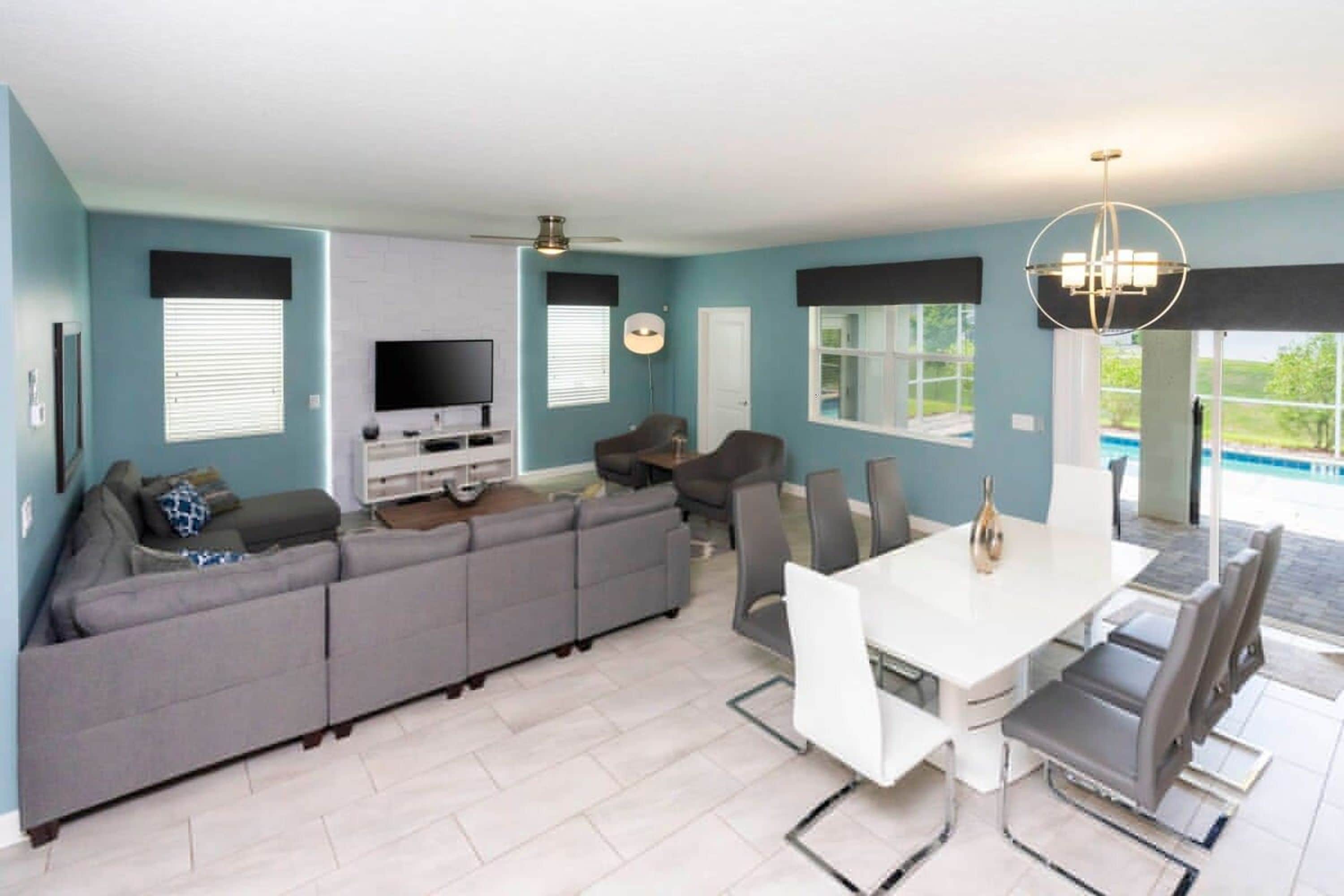 Un salon moderne comprenant un canapé d’angle, un téléviseur à écran plat, une table à manger avec des chaises et un ventilateur de plafond.