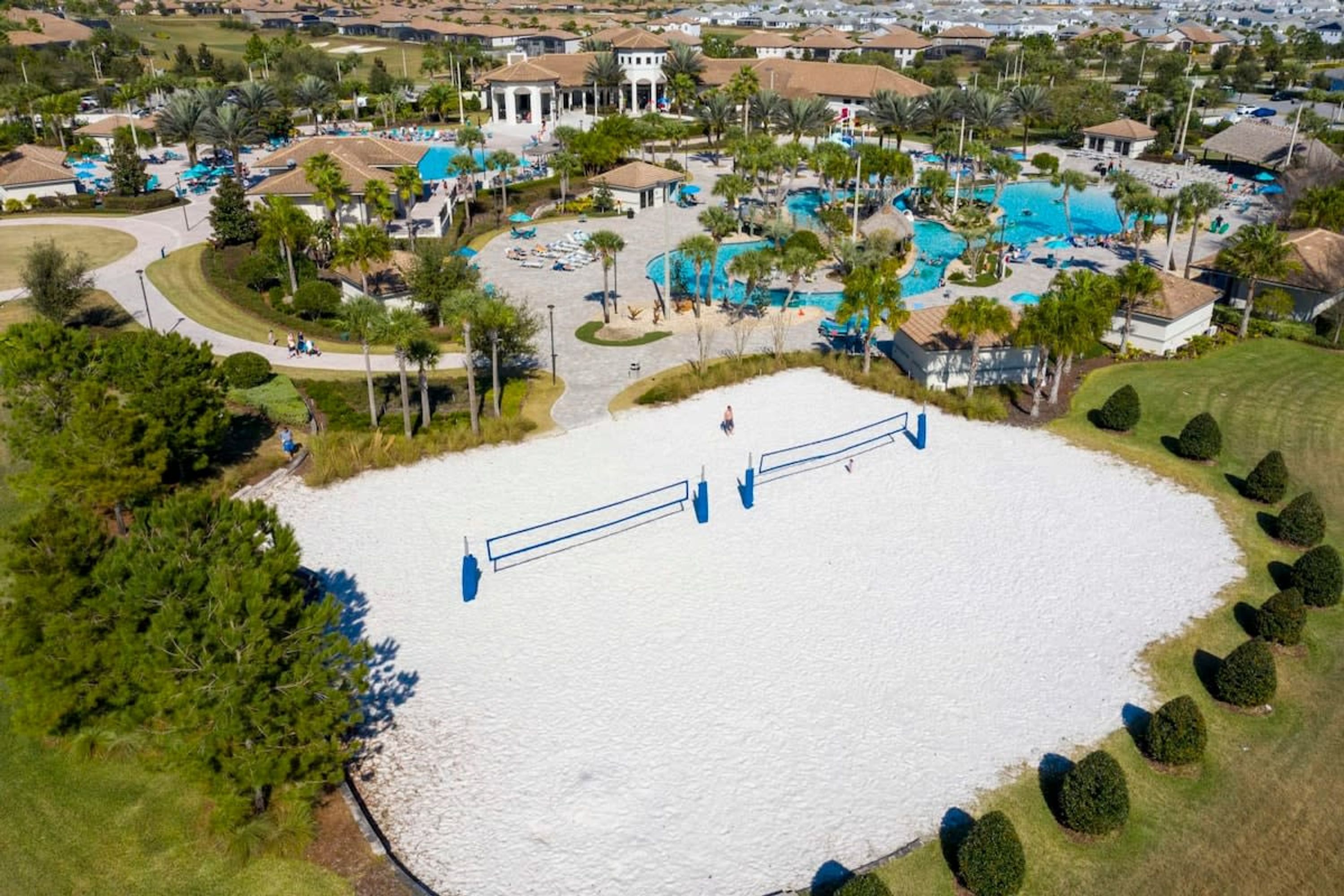An aerial view of a resort with multiple swimming pools, a central white sand area, and surrounding greenery.