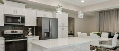 Una cocina moderna con armarios blancos, electrodomésticos de acero inoxidable y una isla central con taburetes de bar.