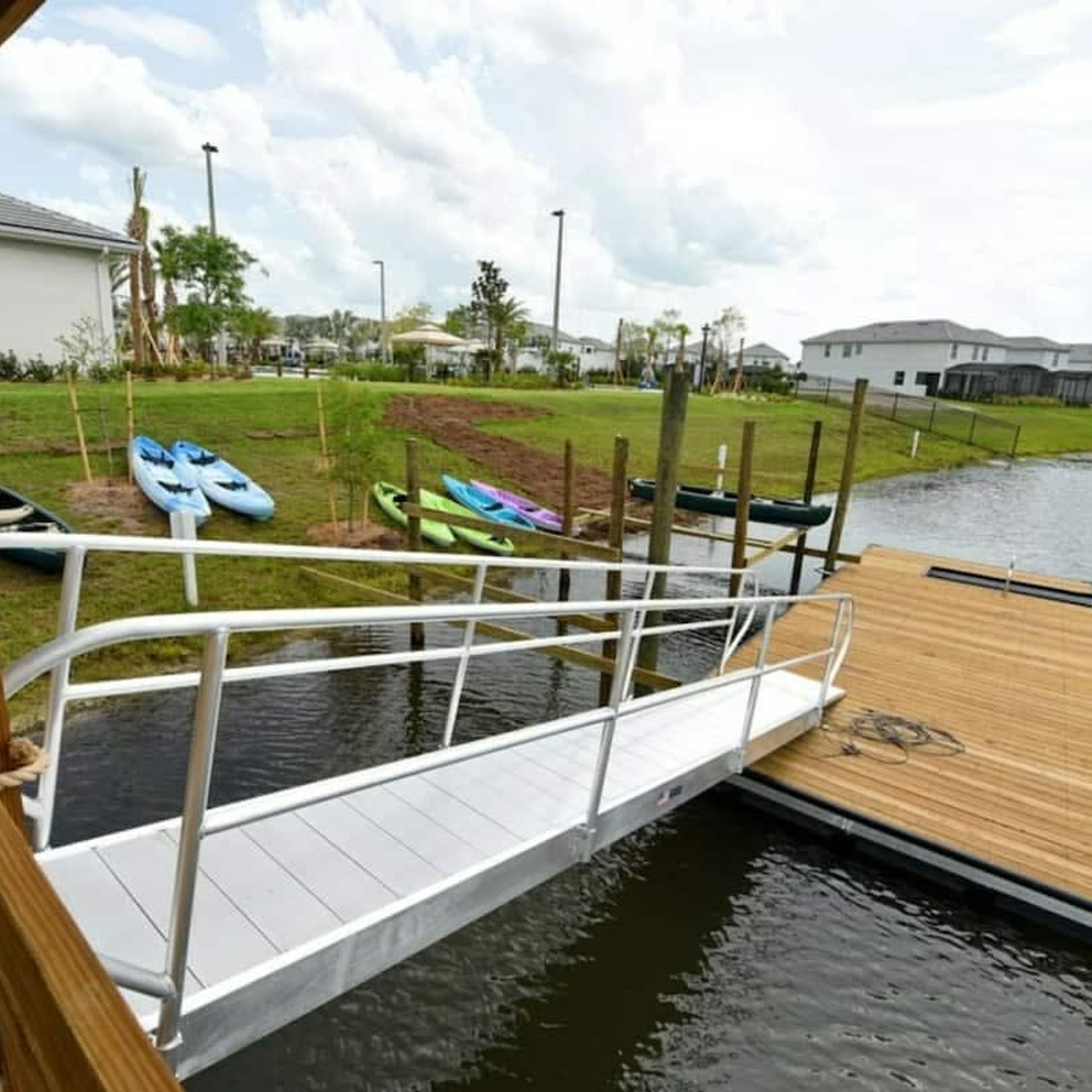 A wooden dock extending over a calm body of water, with a small white bridge leading to a grassy area.