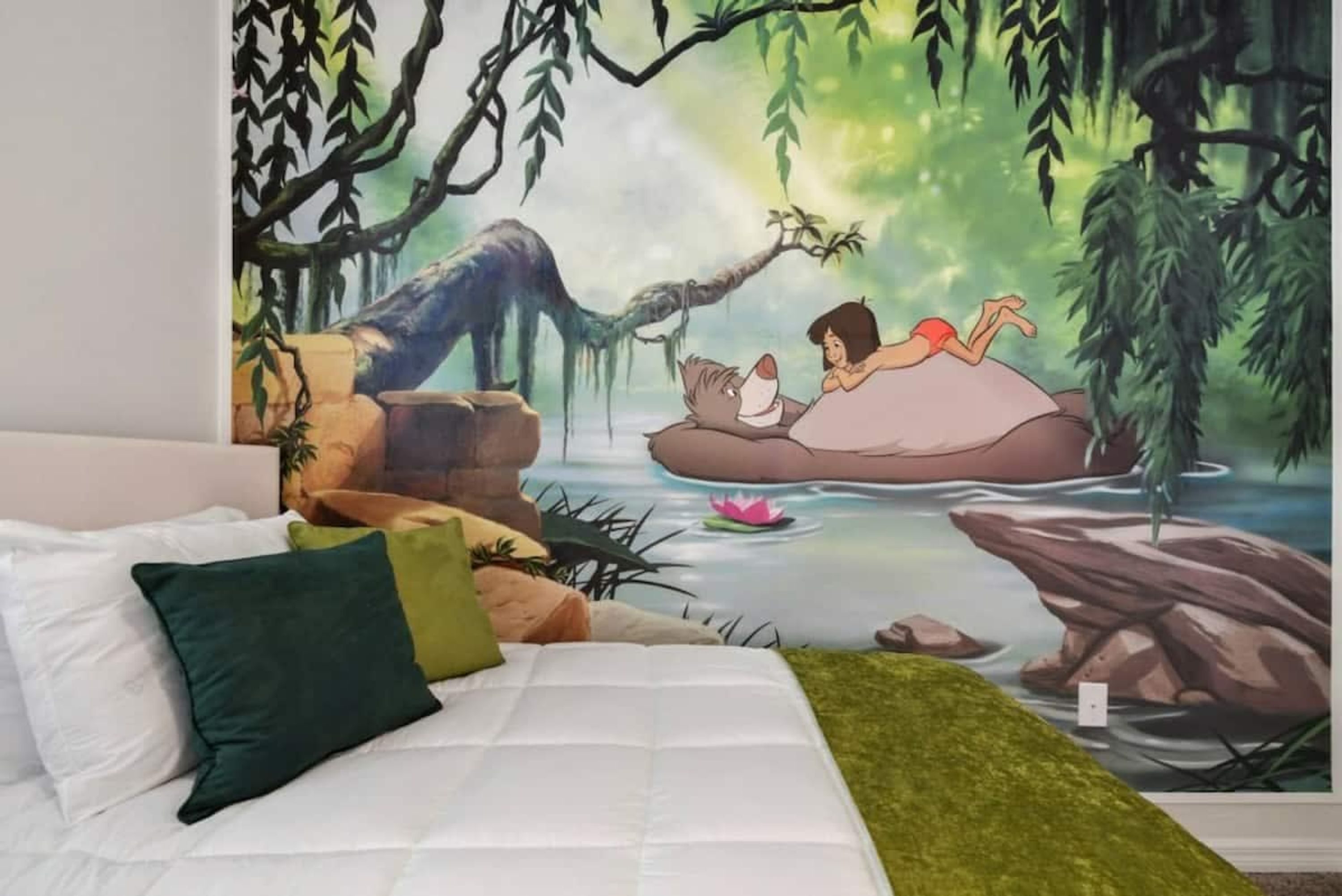 Un dormitorio con un mural de una escena boscosa, una cama con almohadas y una manta verde.