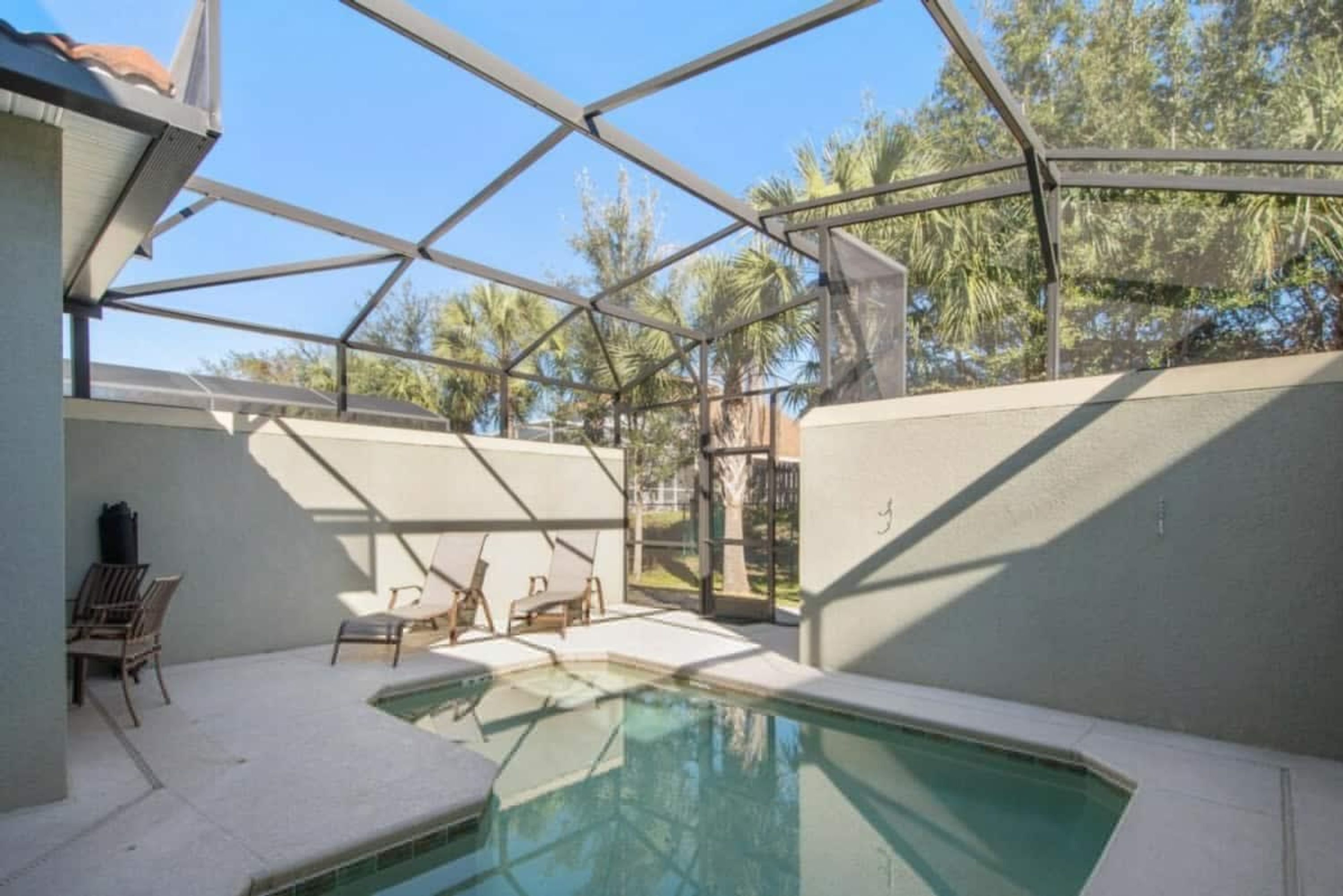 A covered outdoor swimming pool with a metal roof, surrounded by walls and a few lounge chairs.