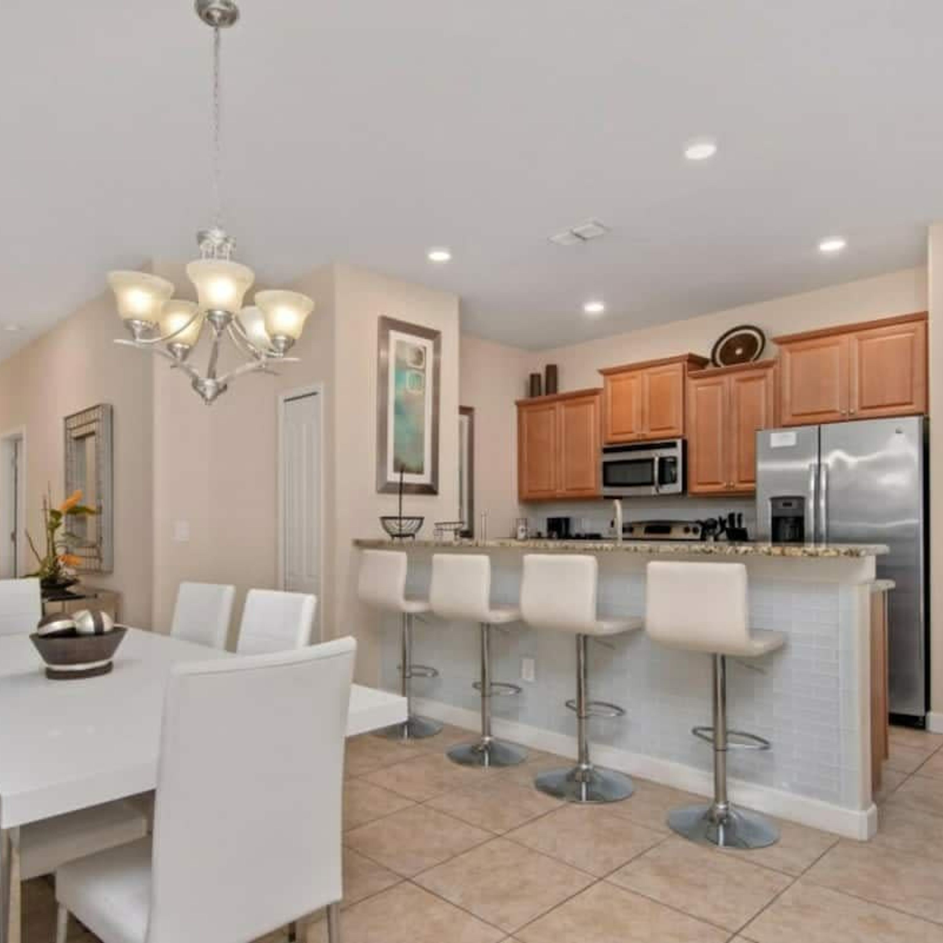 A modern kitchen with a central island, bar stools, and a dining area with a chandelier.