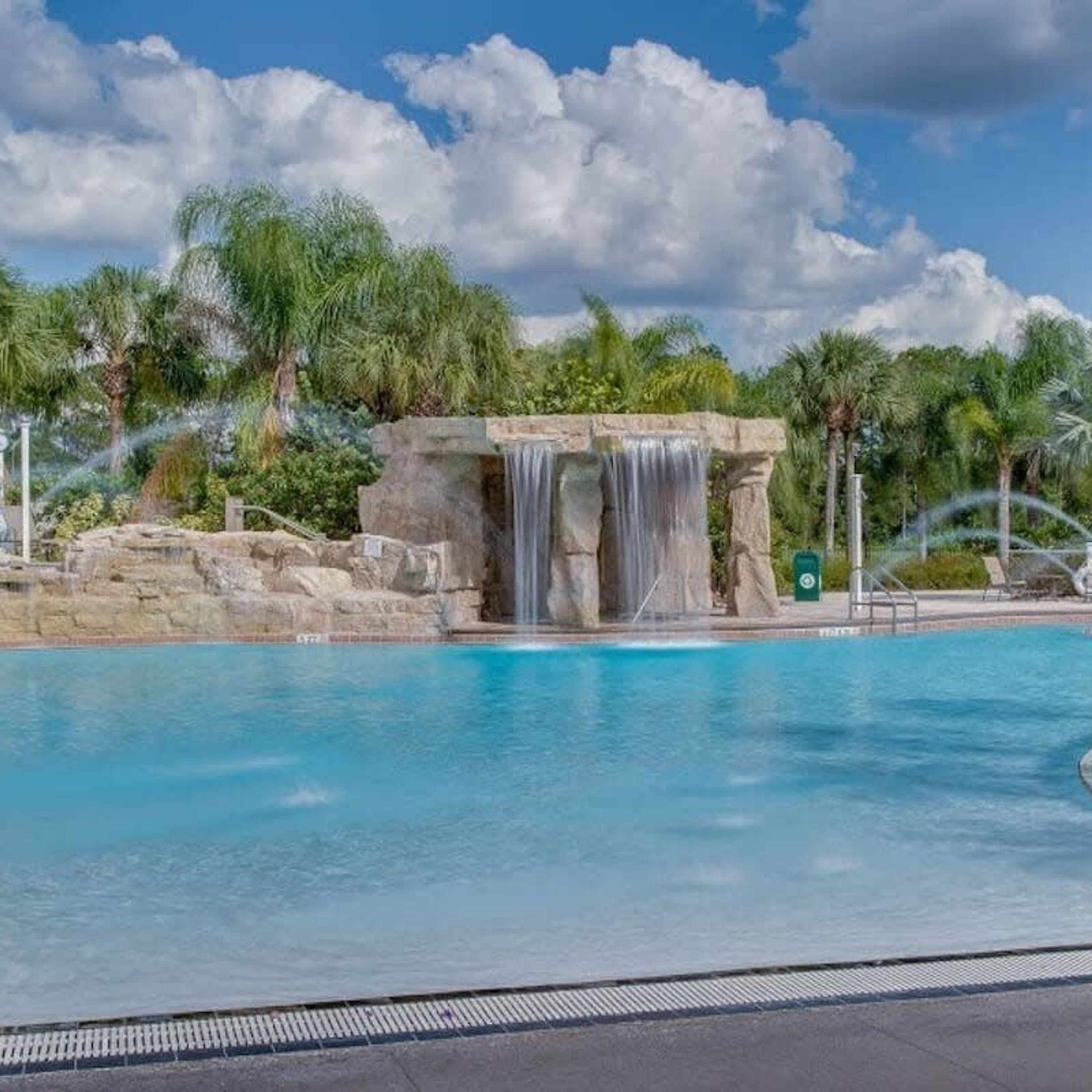 A pool with a waterfall feature, surrounded by palm trees and a clear sky.