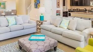 A modern living room with two sofas, a coffee table, and a kitchen area with dark cabinets and a sink. - 9004 Amazing 5BD With Pool (Kissimmee)