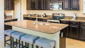 A kitchen with dark cabinets, a central island with bar stools, a microwave, and a stove. - 9004 Amazing 5BD With Pool (Kissimmee)