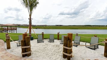 A beach area with lounge chairs and a palm tree, overlooking a body of water and distant buildings.