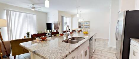 Una cocina moderna con encimera de granito, electrodomésticos de acero inoxidable y un comedor con televisor.