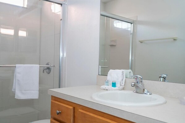 A modern bathroom with a glass shower enclosure, a white sink with a mirror above it, and a wooden vanity with drawers.