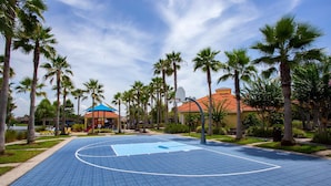 An outdoor basketball court surrounded by palm trees and a building with a red roof. - 133 Beautiful 5BD Home With Lake View (Kissimmee)