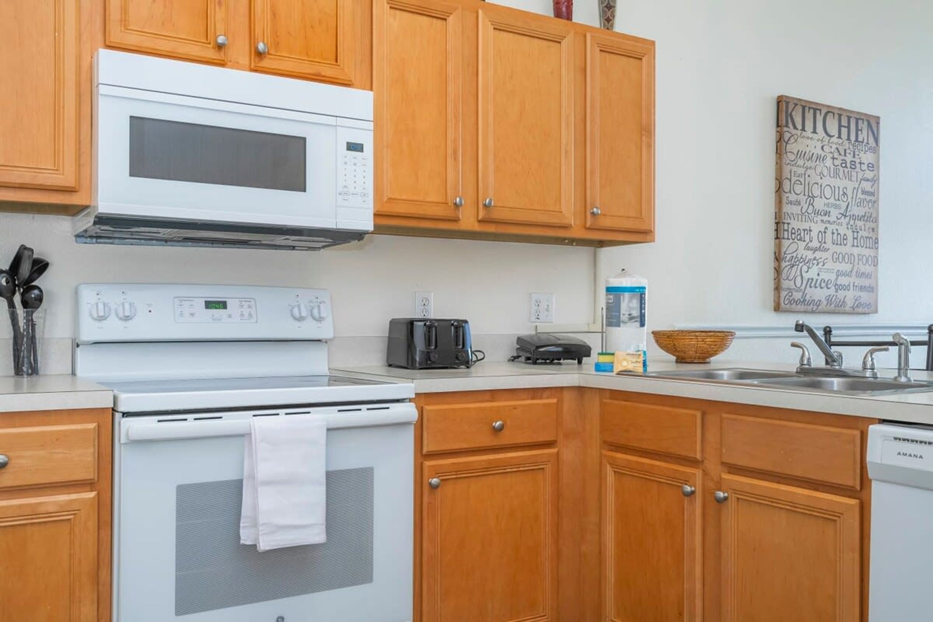 Une cuisine avec des meubles de rangement en bois, une cuisinière blanche, un four à micro-ondes, un grille-pain et un lave-vaisselle.