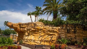 A rock wall with the inscription "Tierra Verde" surrounded by tropical plants and palm trees. - 133 Beautiful 5BD Home With Lake View (Kissimmee)