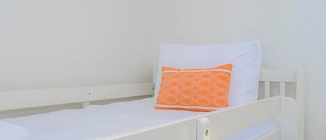 A single white bed with an orange patterned pillow and a white pillow.