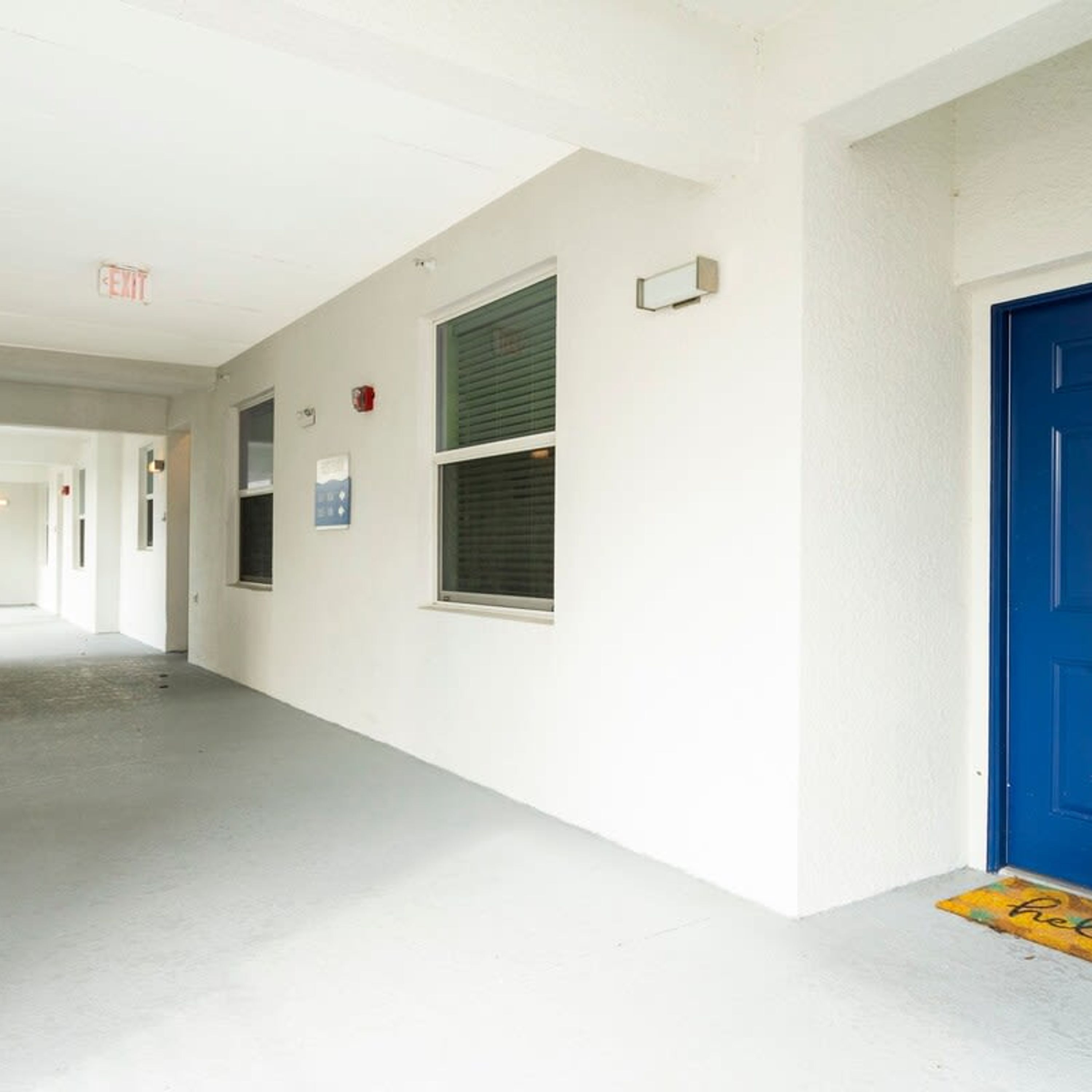 A hallway with white walls, a blue door, and a yellow doormat with "hello" written on it.
