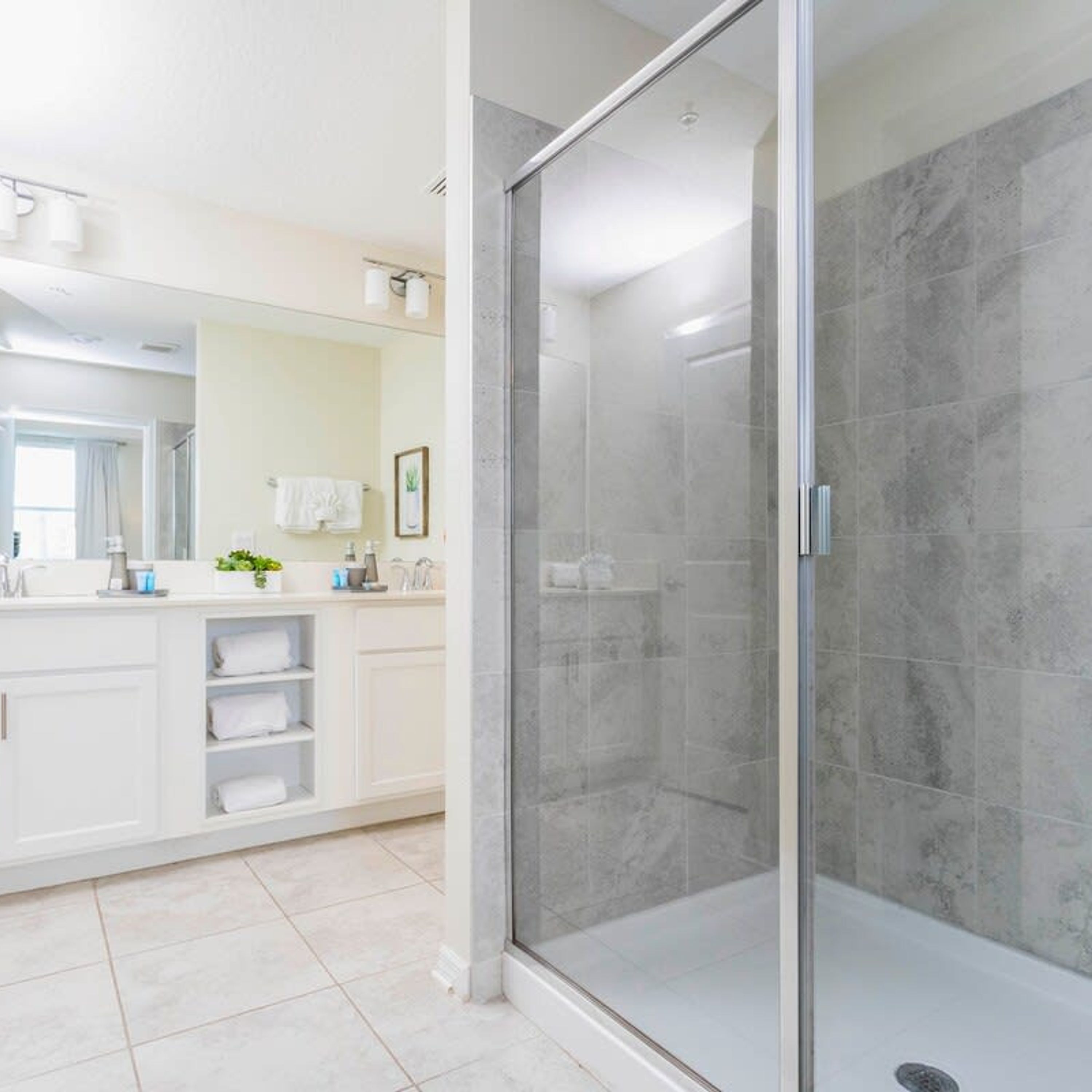 A modern bathroom with a glass-enclosed shower, white cabinetry, and a large mirror.