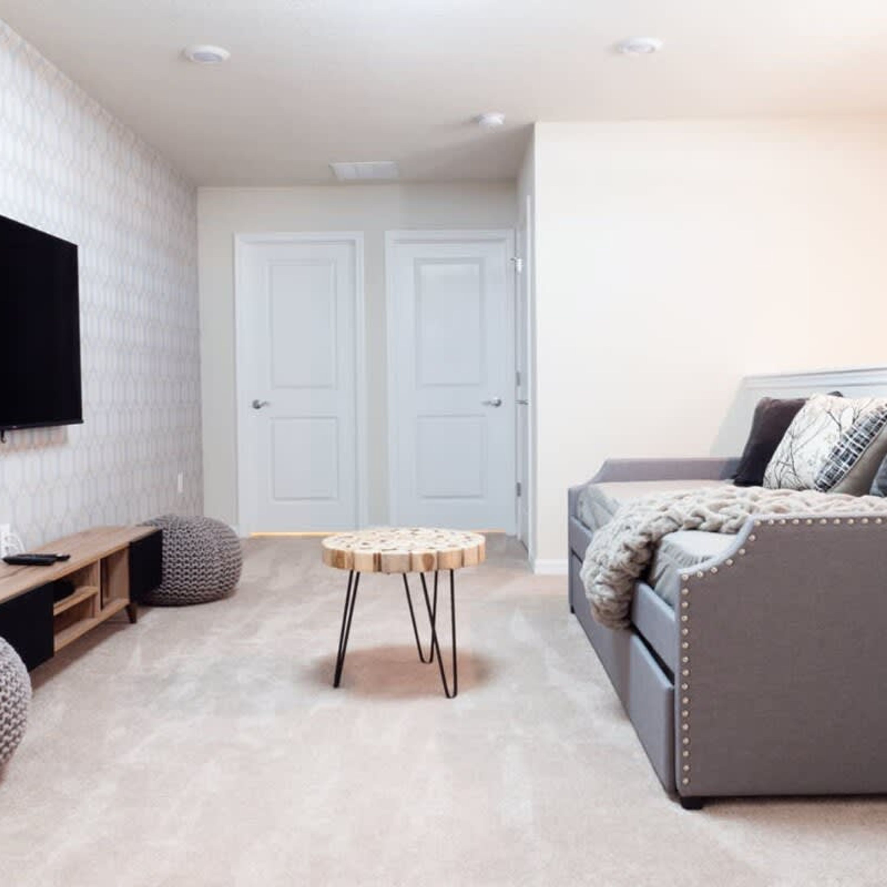 A modern living room with a grey sofa, a round wooden coffee table, and a flat-screen TV mounted on the wall.