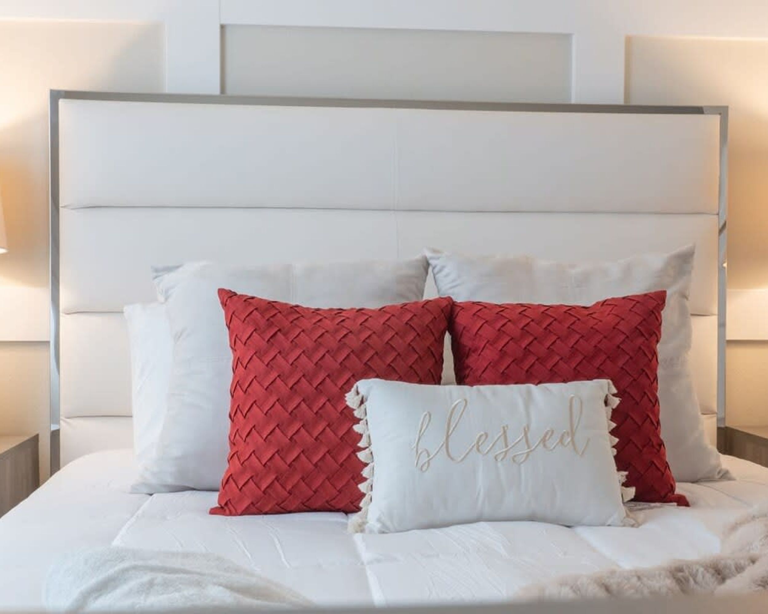 A bed with a white headboard, white bedding, and two red pillows with a woven texture.