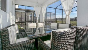 Eine sonnendurchflutete Terrasse mit Korbmöbeln, einem Glastisch und einem Deckenventilator.