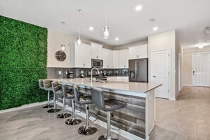 Eine moderne Küche mit grüner Wand, Edelstahlgeräten und einer Bar mit Hockern.