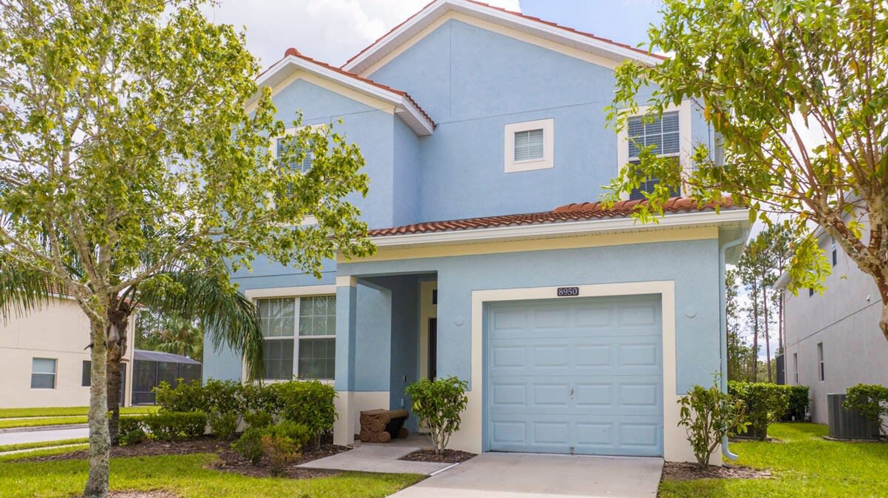A two-story residential house with a light blue exterior, a red-tiled roof, and a garage door.