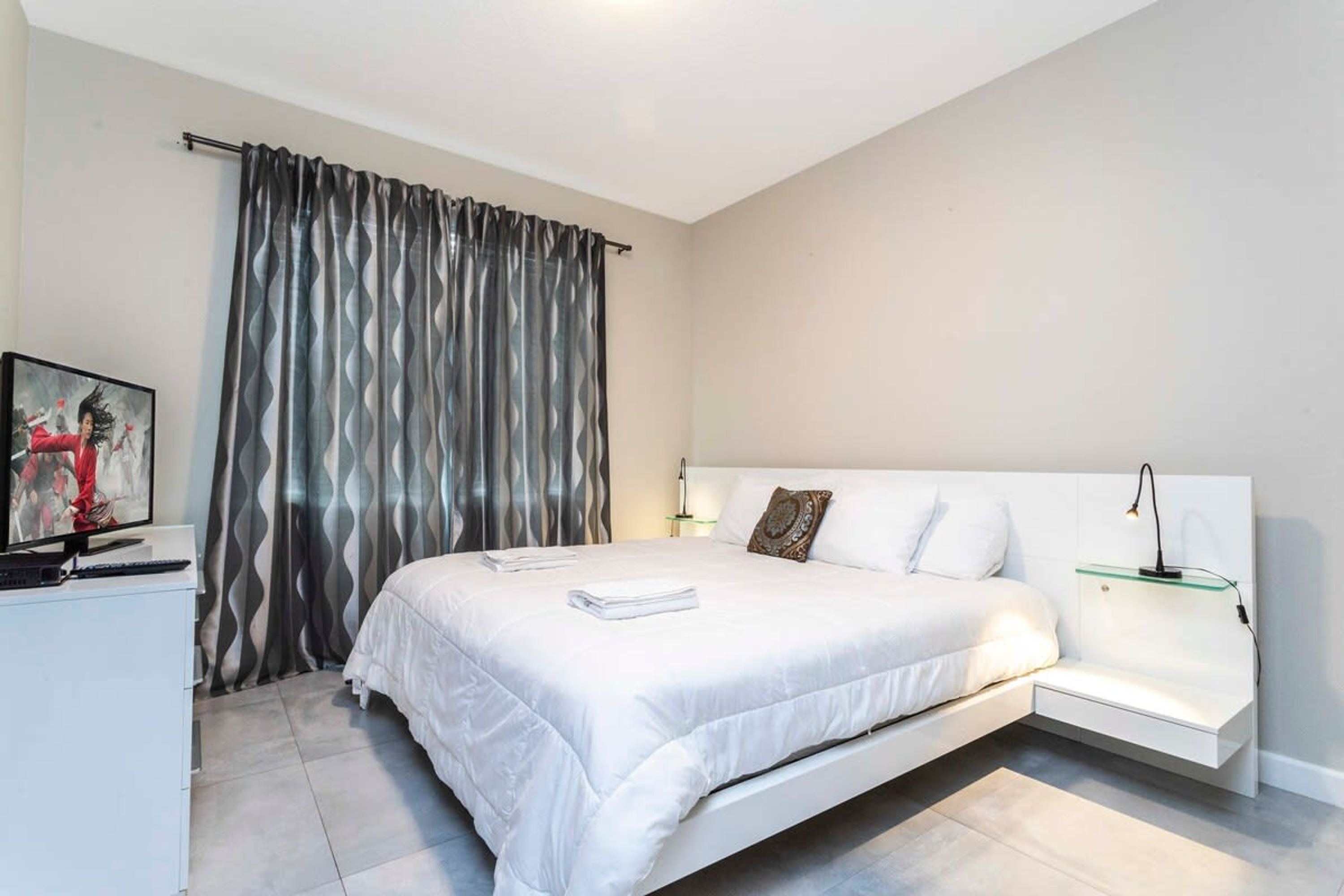 A modern bedroom with a bed, a bedside table, a TV, and a curtain.