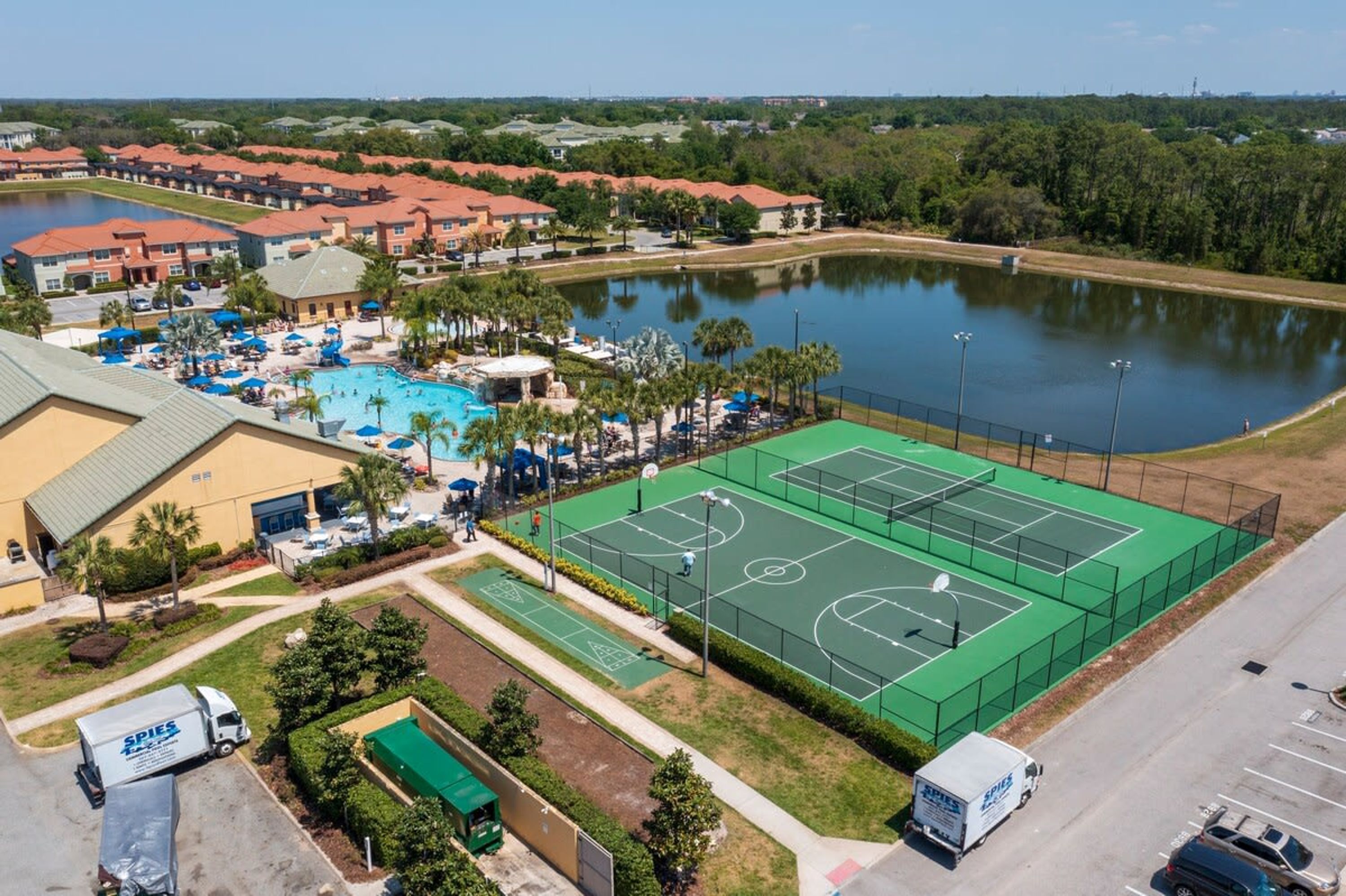 An aerial view of a resort with a swimming pool, tennis courts, and a lake.