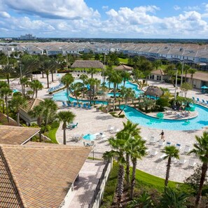 A resort with a large swimming pool, palm trees, and a view of the surrounding buildings.