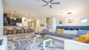 A modern living room with a glass coffee table, a sofa with cushions, a marble-patterned rug, and a kitchen in the background. - 1400 Stunning 8BD With Amazing Game Room (Davenport)
