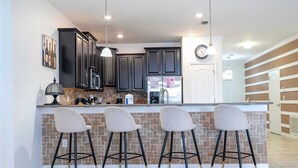 A modern kitchen with dark cabinets, a central island with bar stools, and a clock on the wall. - 1400 Stunning 8BD With Amazing Game Room (Davenport)