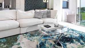Un salon moderne avec une table basse en verre, un canapé blanc et un tapis à motifs.