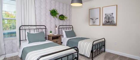 A bedroom with two twin beds, a nightstand, a wall-mounted plant, and two framed pictures.