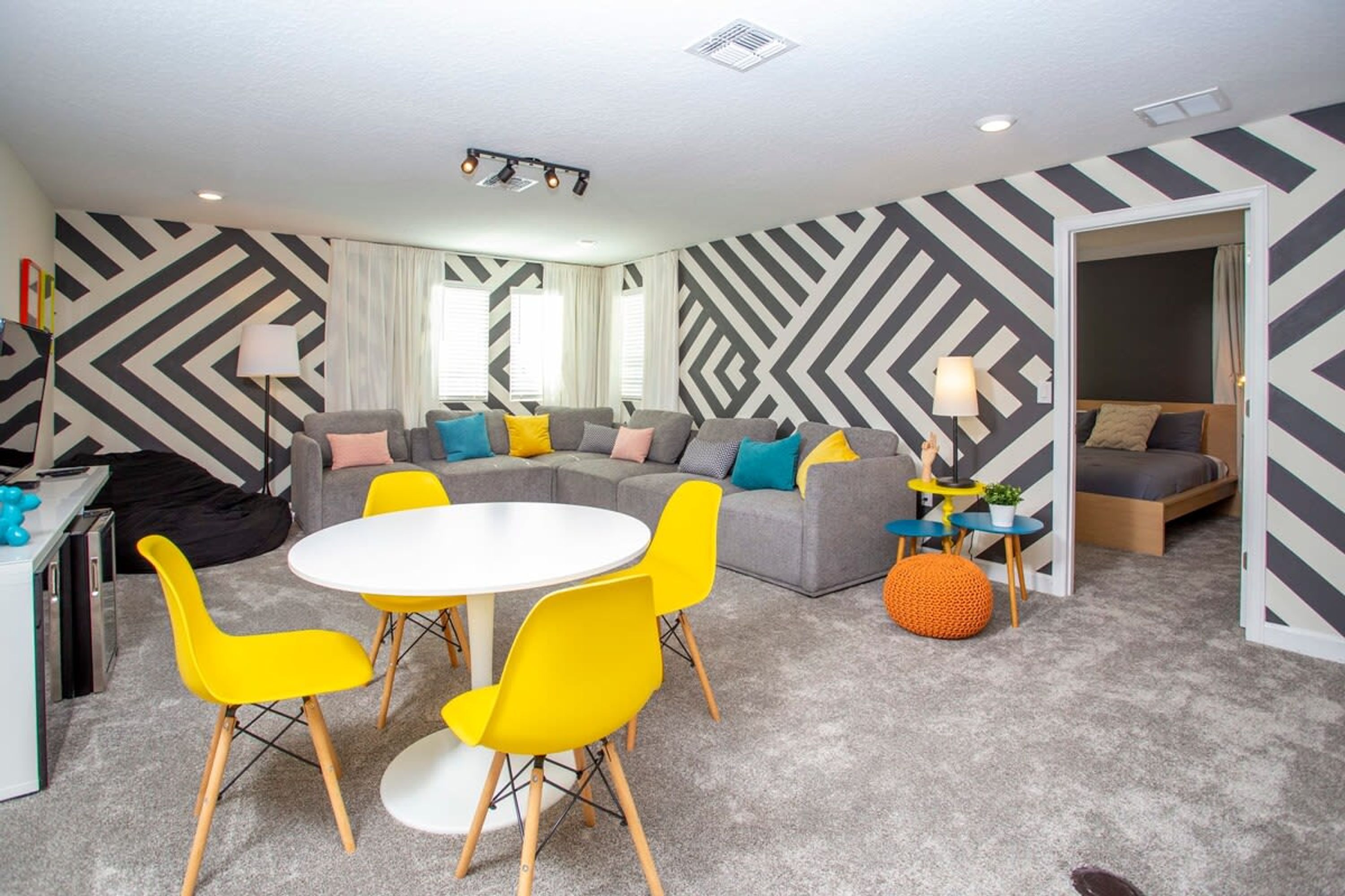 A modern living room with a sectional sofa, a round dining table with yellow chairs, and a small side table with a lamp.