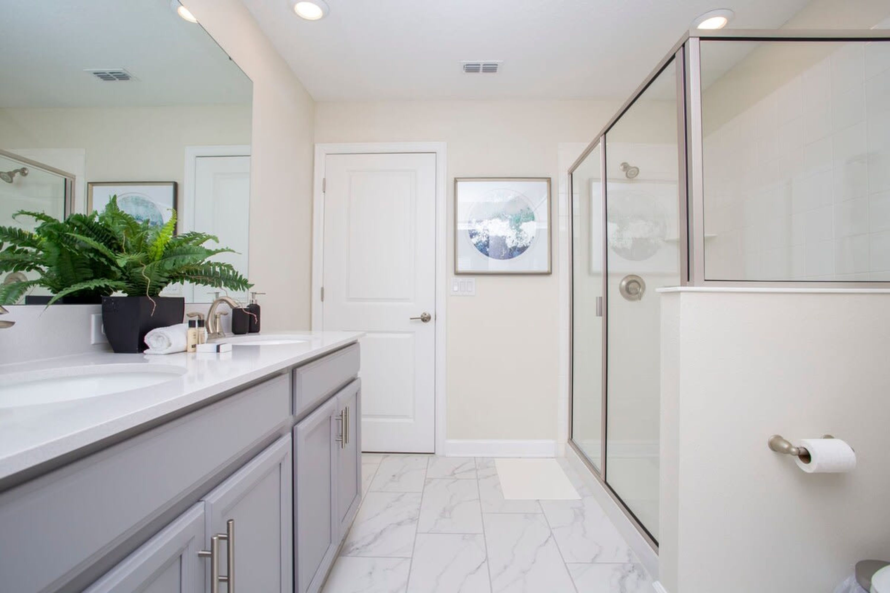 A modern bathroom with a large mirror, a shower enclosure, and a marble floor.