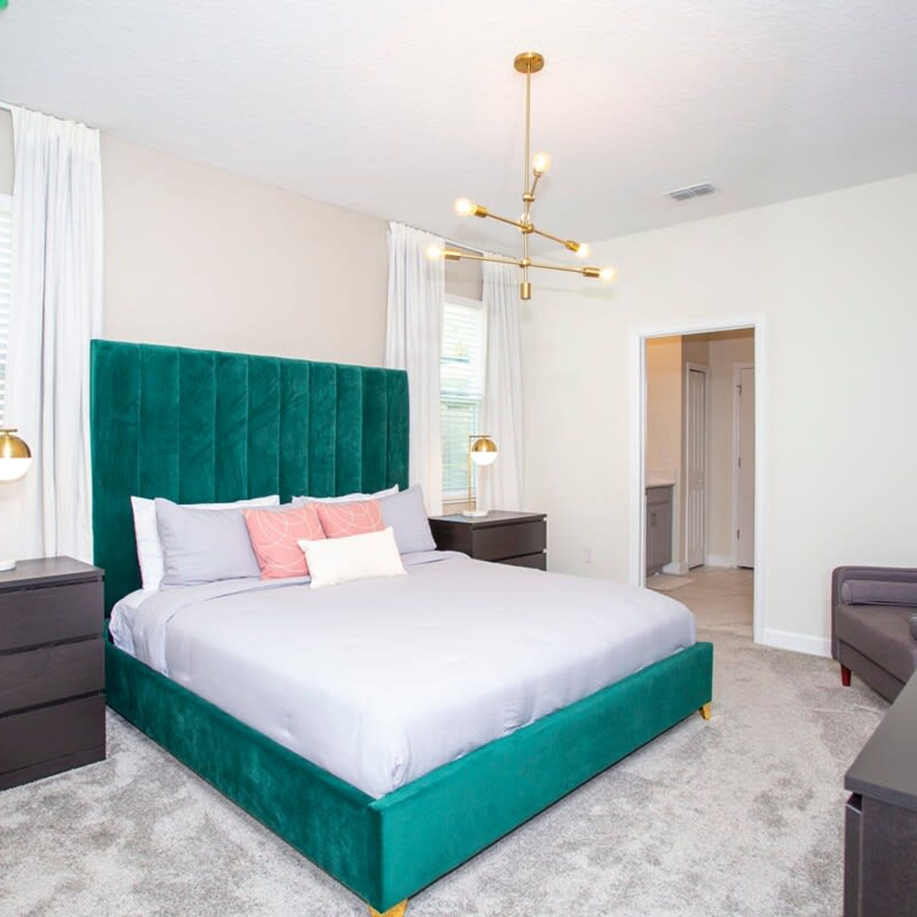A modern bedroom with a teal upholstered bed, white bedding, and a unique chandelier.
