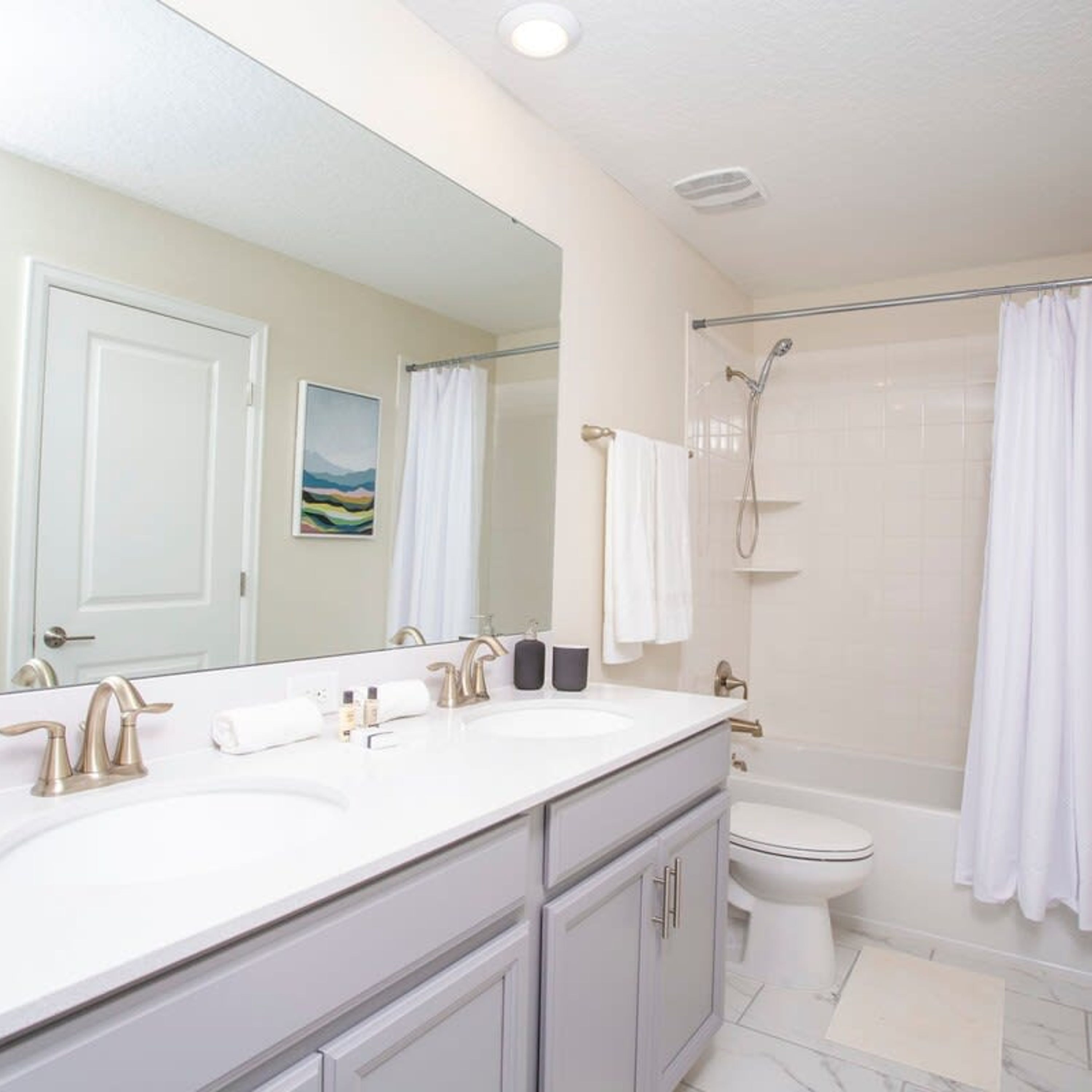 Un bagno moderno con un doppio lavabo, uno specchio grande, una doccia con porta in vetro e un water.